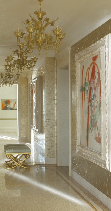 Luxurious hallway with ornate chandeliers, abstract paintings, and a cushioned bench on a reflective tiled floor.