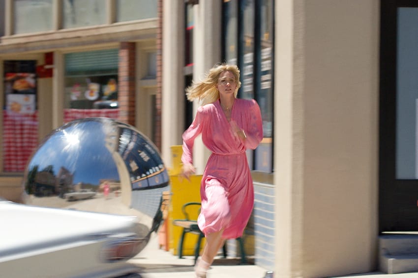 Woman in a pink dress running down a street past a fire hydrant and a large reflective mirror.