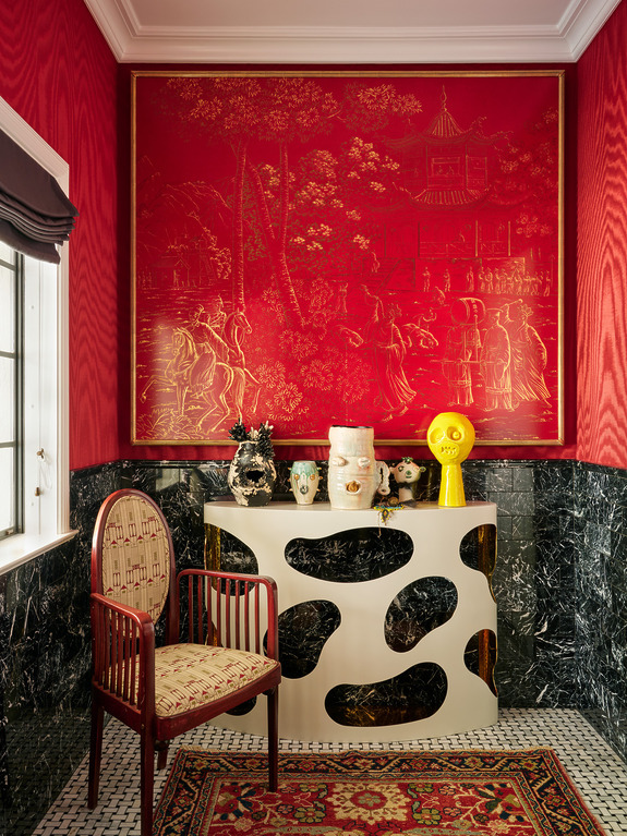 Eclectic room with red walls, abstract console table, decorative vases, modern art, and patterned chair near window.
