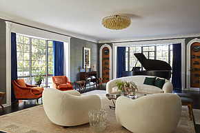 Elegant living room with white sofas, orange chairs, a grand piano, and large windows with blue curtains.