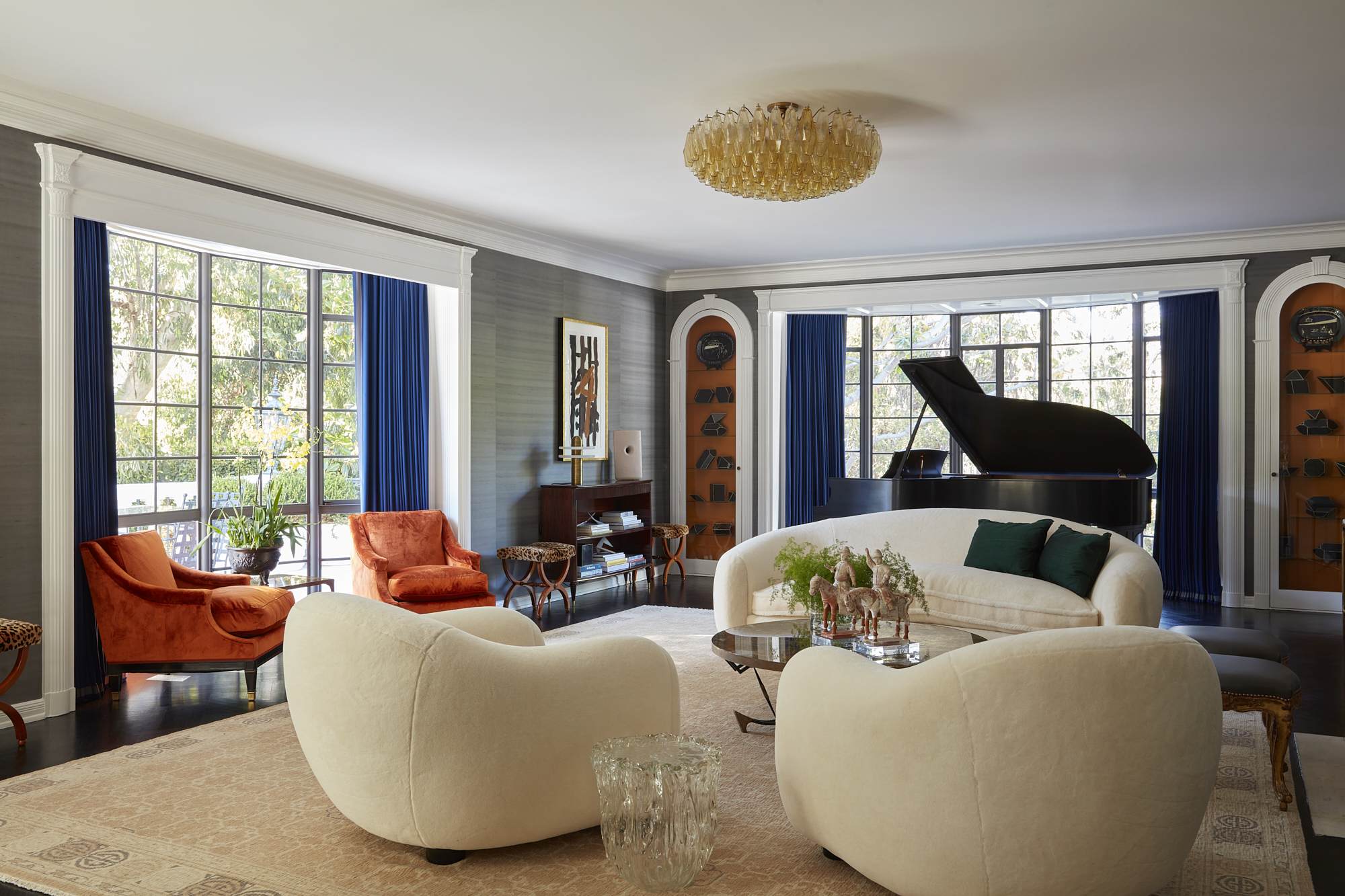 Elegant living room with white sofas, orange chairs, a grand piano, and large windows with blue curtains.