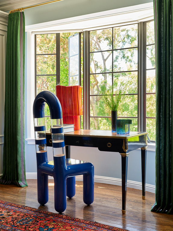 Colorful modern chair and elegant desk in a room with large windows and green curtains, natural light illuminating the space