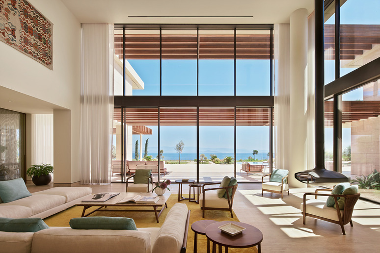 Spacious living room with large windows overlooking patio and ocean, featuring modern furniture and neutral decor.