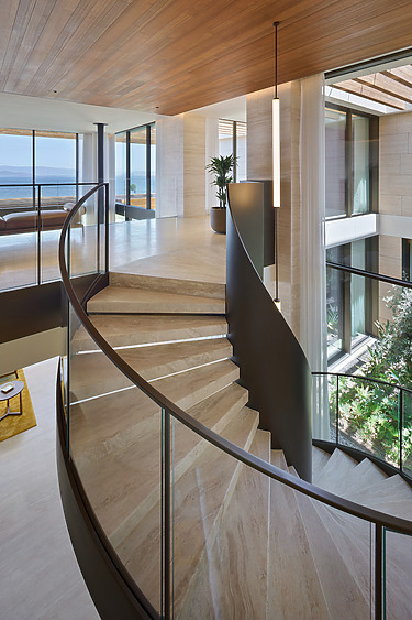Modern interior with curved staircase, wooden ceilings, floor-to-ceiling windows, and ocean view in a luxury home.