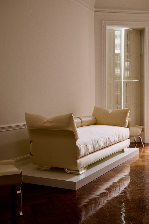 A cream-colored modern sofa with cushions on a wooden floor in a warmly lit room with an open window nearby