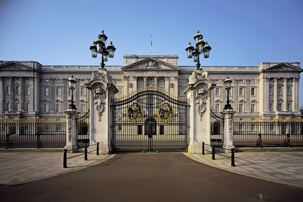 Exterior view of Buckingham Palace with ornate gates and clear blue sky in the background.