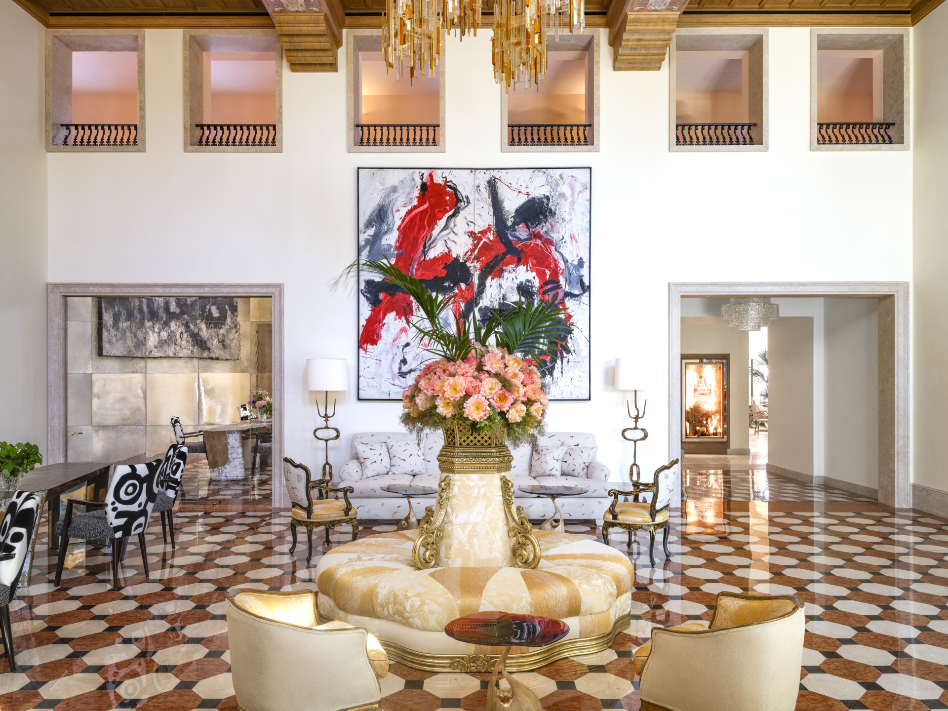 Luxurious hotel lobby with elegant furniture, vibrant artwork, large floral arrangement, and patterned floor tiles.