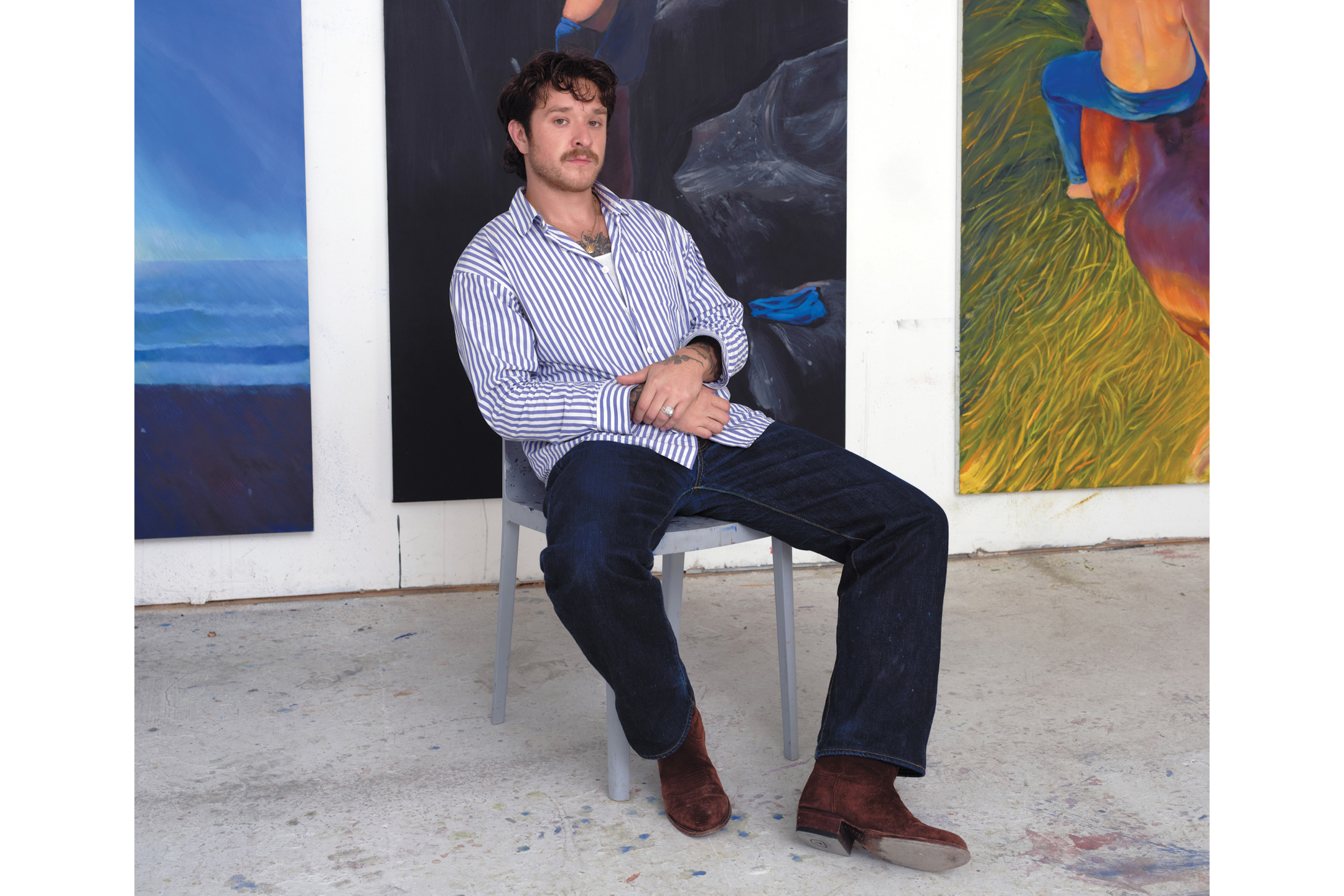 Man sitting on chair in art studio with paintings in the background.