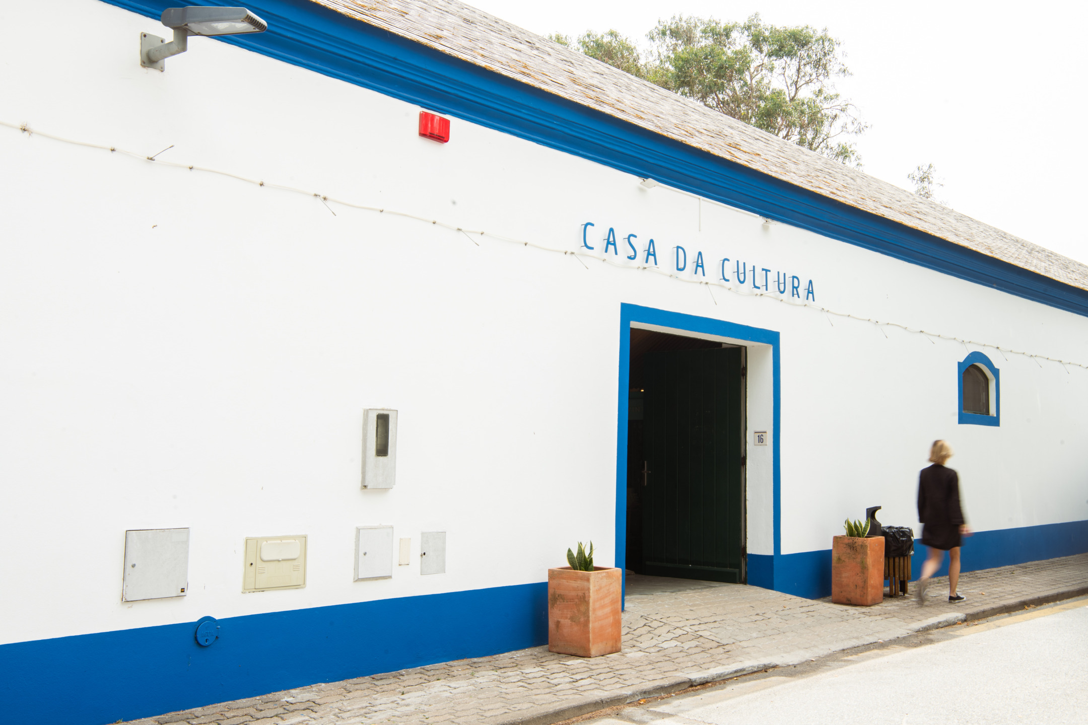 White building with blue trim labeled "Casa da Cultura," entrance open, person walking past.