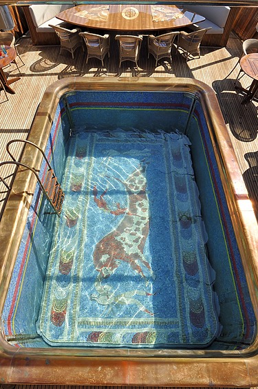 Rectangular pool with a mosaic of a giraffe at the bottom, surrounded by wooden outdoor dining furniture.