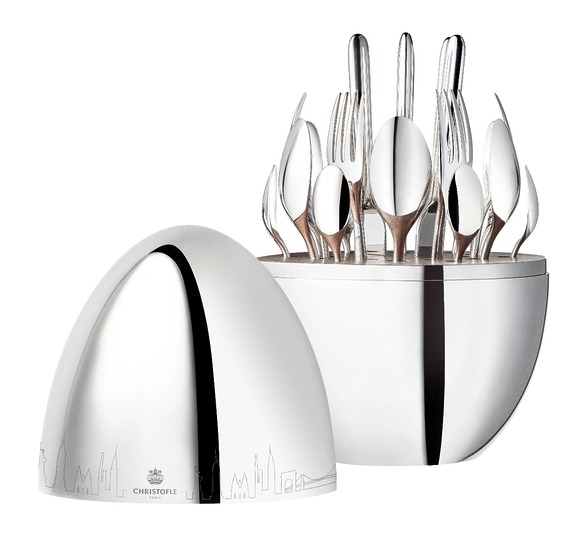 Silver Christofle egg flatware set with utensils displayed and closed egg in background featuring engraved city skyline design