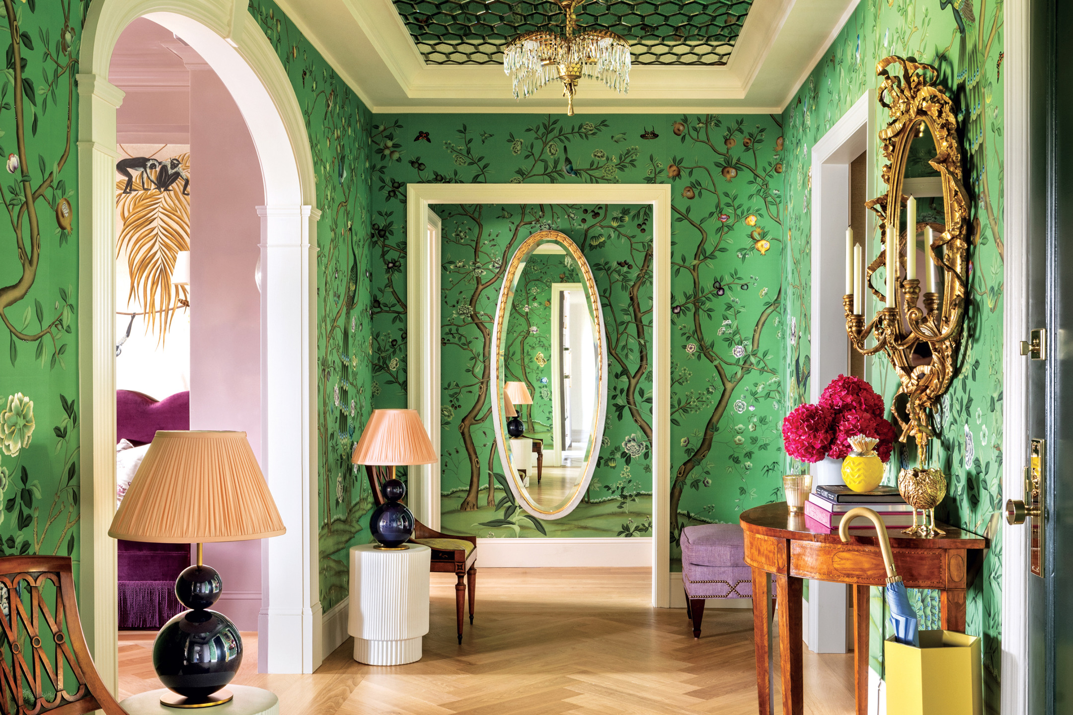 Colorful hallway with green wallpaper, oval mirror, arched doorway, chandelier, and elegant furniture.