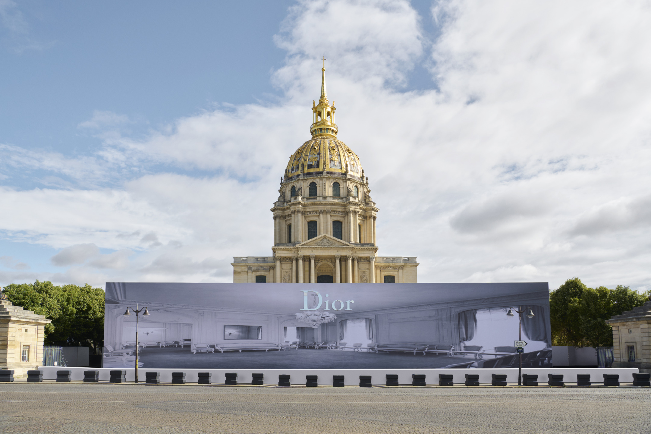 Facade of a historic building with a Dior exhibition poster, under a partly cloudy sky.