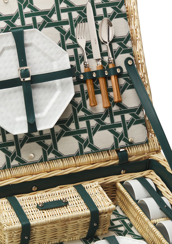 Open picnic basket with green patterned lining, plates, cutlery, and woven compartments showcasing organized picnic essentials.