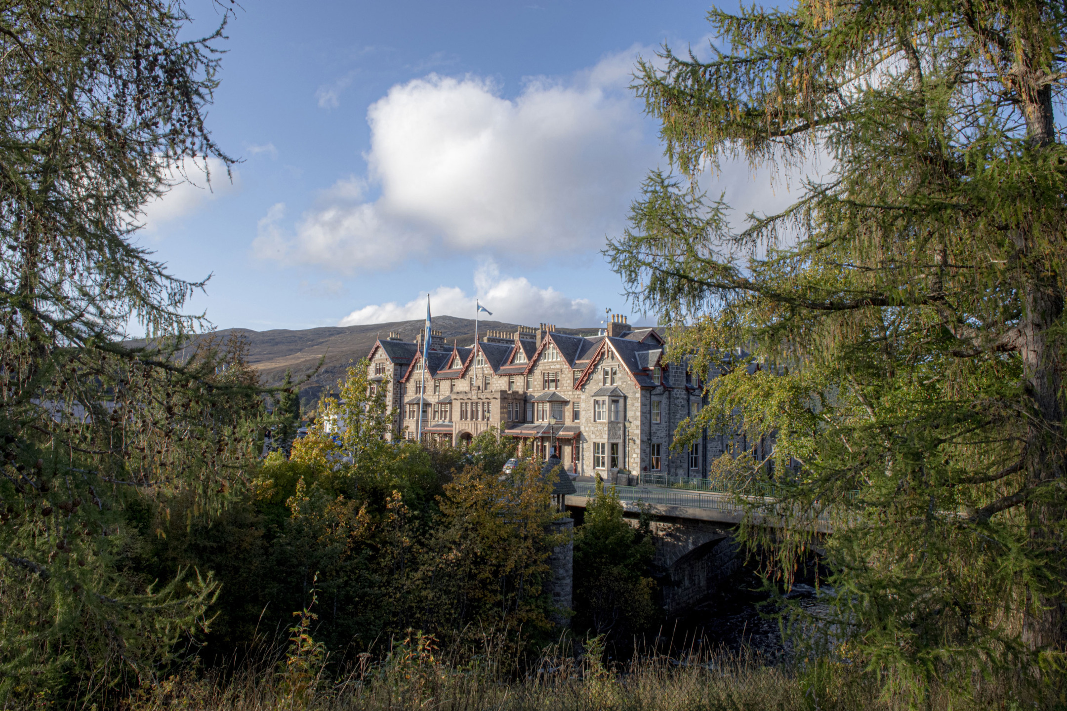 Victorian-style mansion surrounded by trees and hills under a blue sky with clouds.