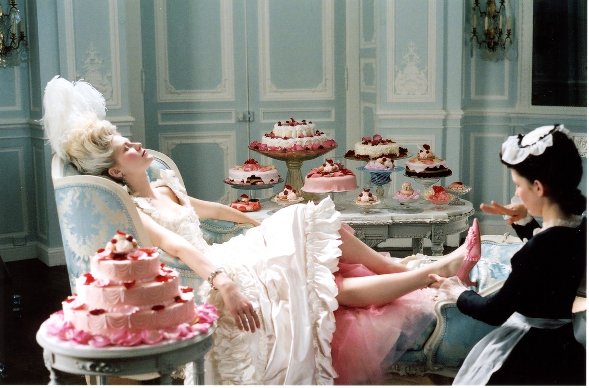 Woman in a lavish gown reclines on a chaise lounge surrounded by ornate cakes, with a maid in attendance.