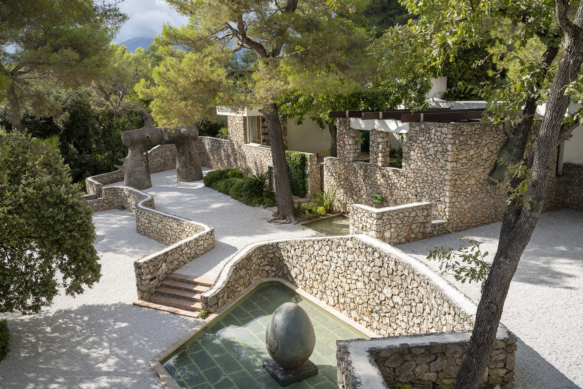 Stone house surrounded by trees and unique sculptures in a garden setting
