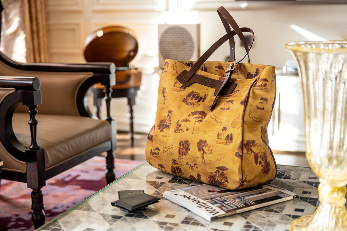 Yellow designer tote bag with brown handles on a table in a luxurious living room, near a magazine and a wallet.