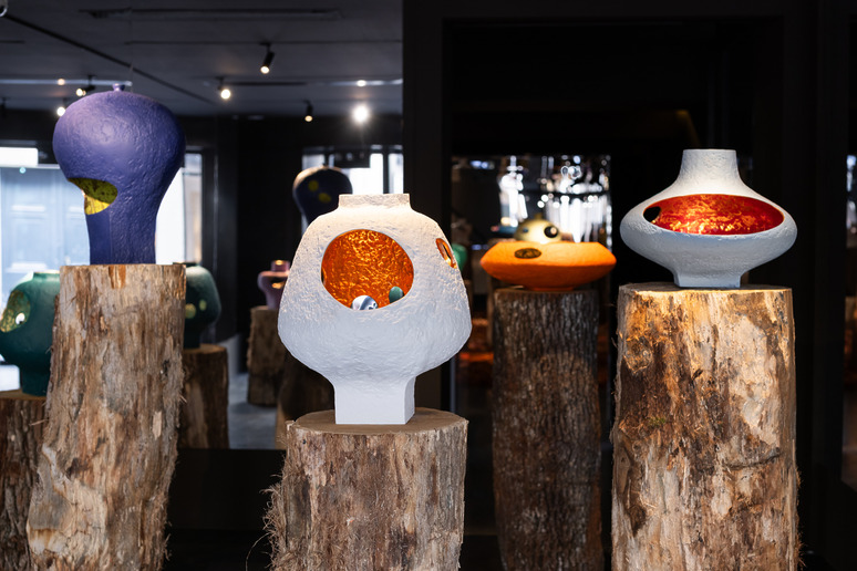 Contemporary art exhibit featuring large, colorful ceramic sculptures displayed on wooden stumps in a dimly lit gallery.