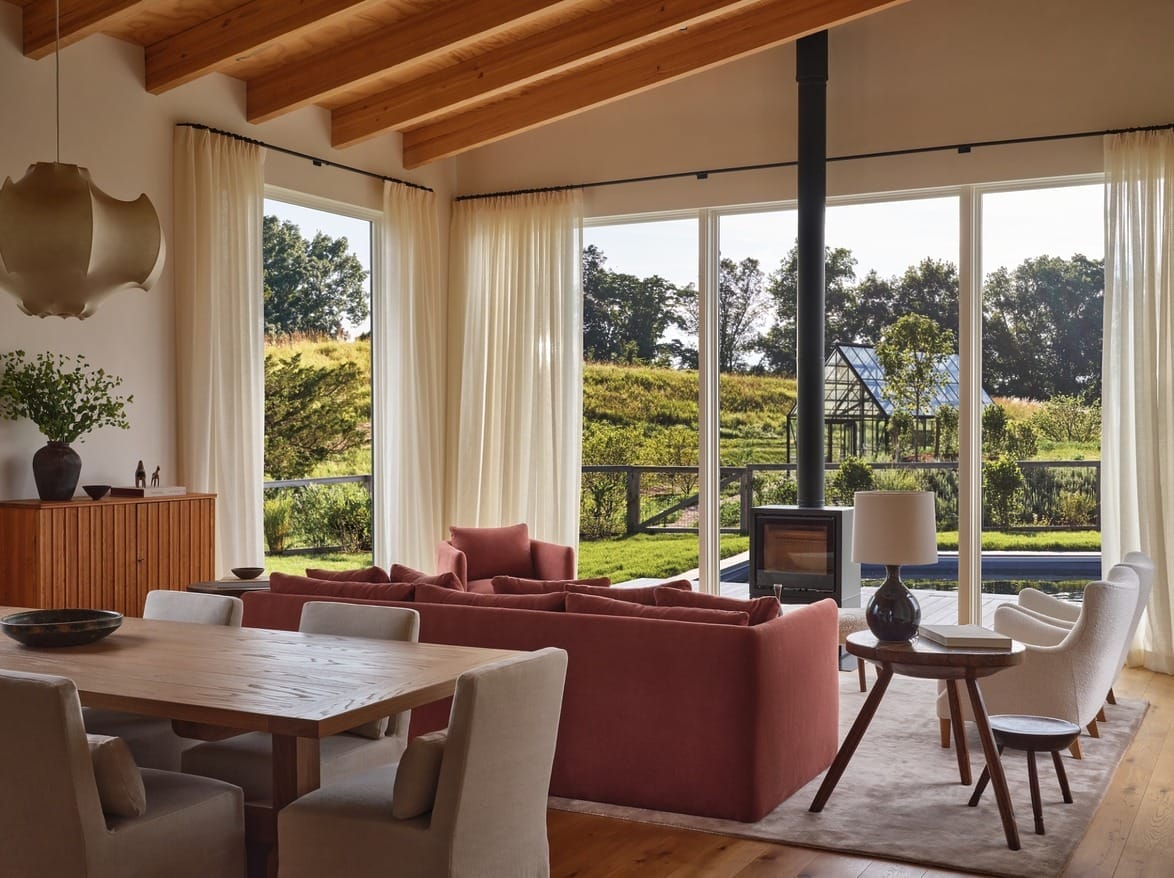 Modern living room with large windows, red sofa, wooden ceiling, and view of lush garden and glass greenhouse.