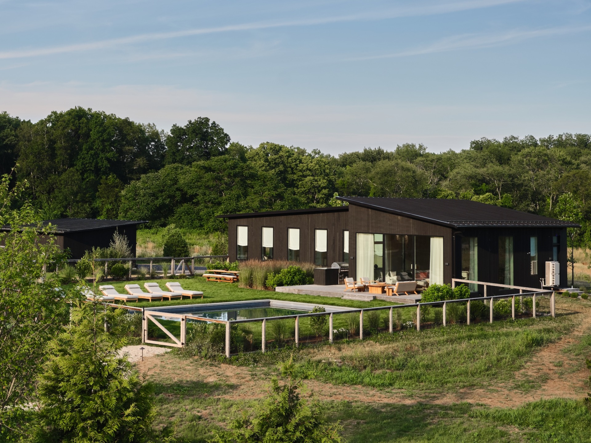 Modern, single-story house with large windows, surrounded by trees, garden, and pool in a scenic outdoor setting.