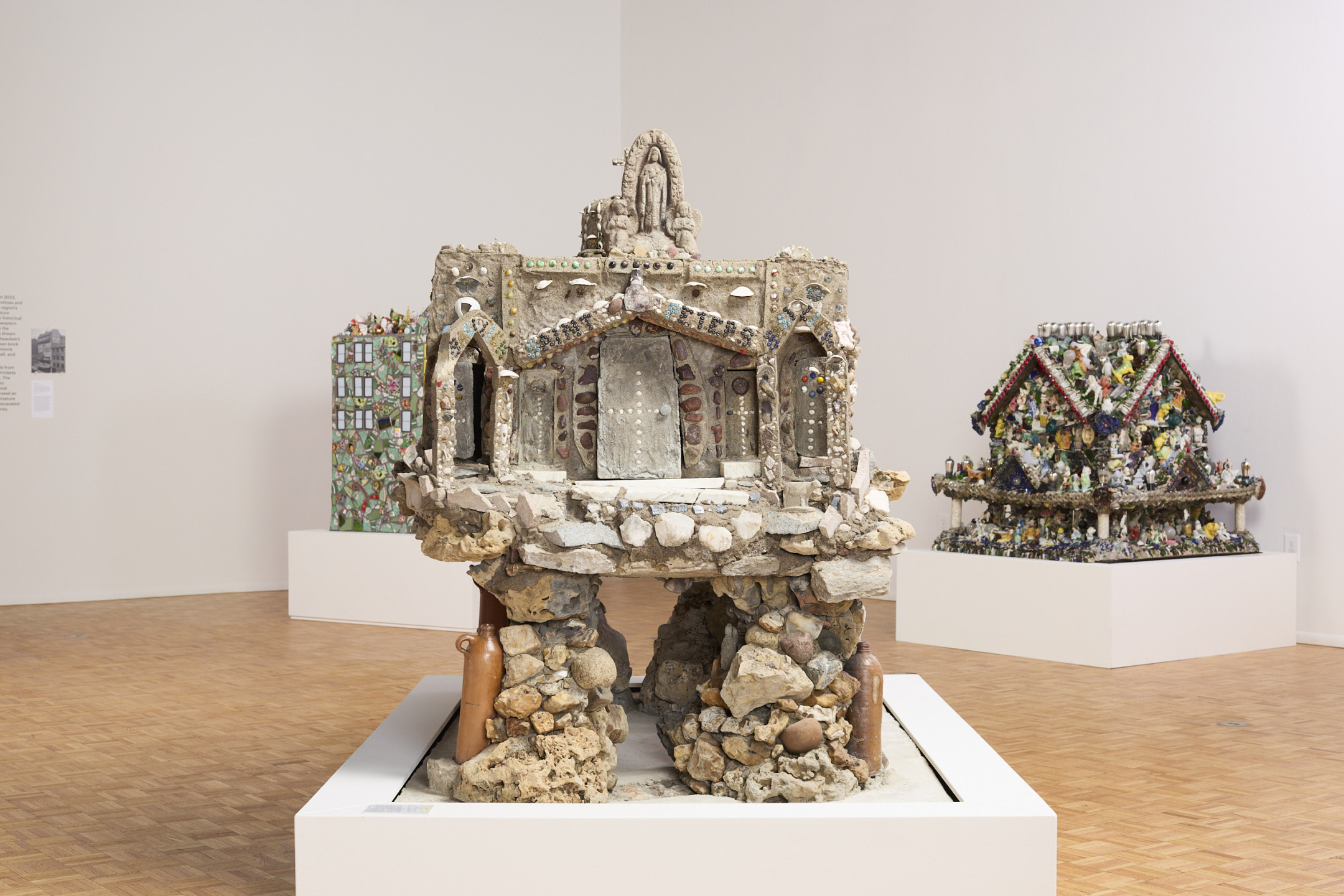 Detailed clay sculptures displayed in a spacious art gallery with wooden flooring and white walls.