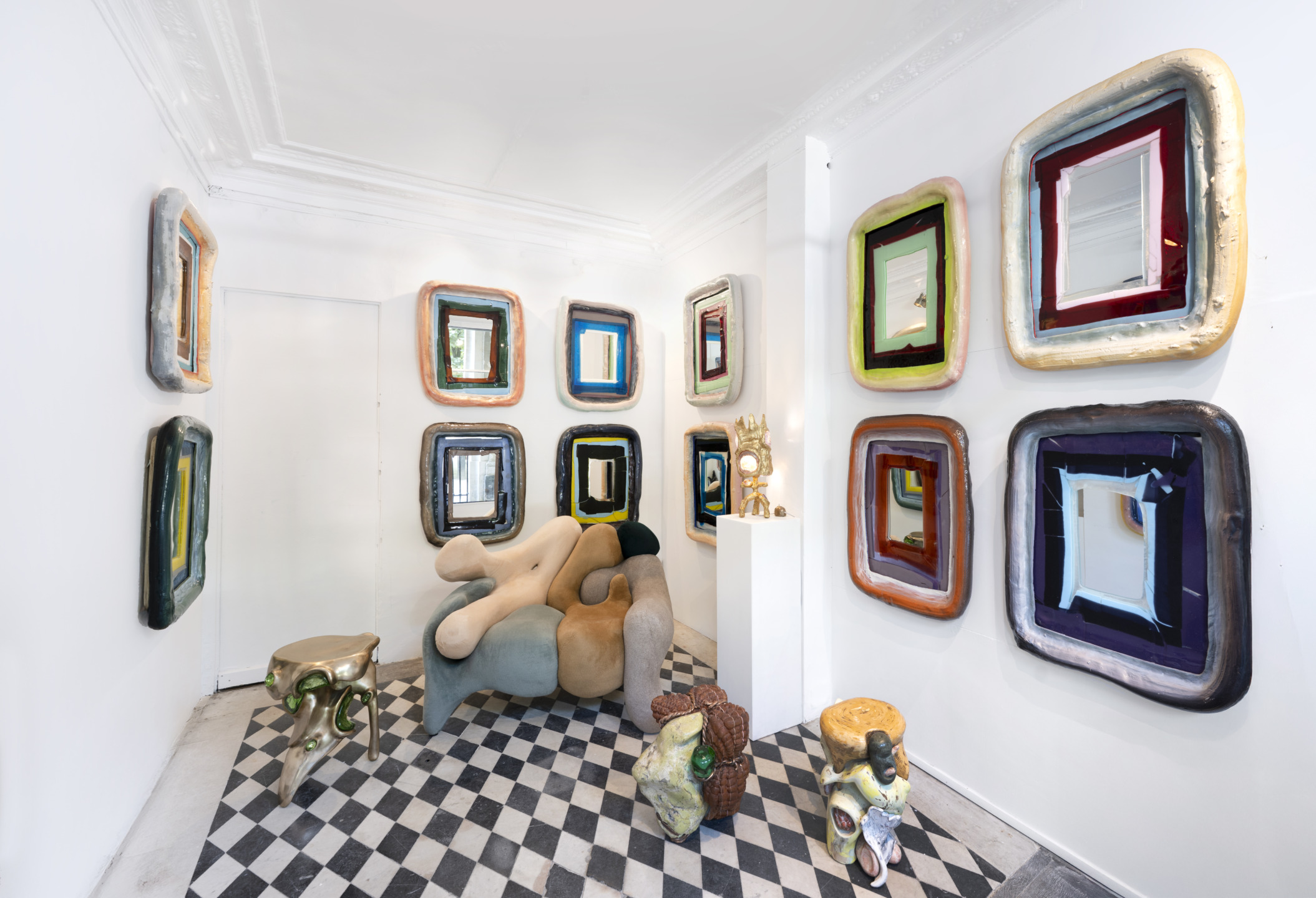 Art gallery with abstract chair, checkered floor, and colorful framed mirrors on white walls.