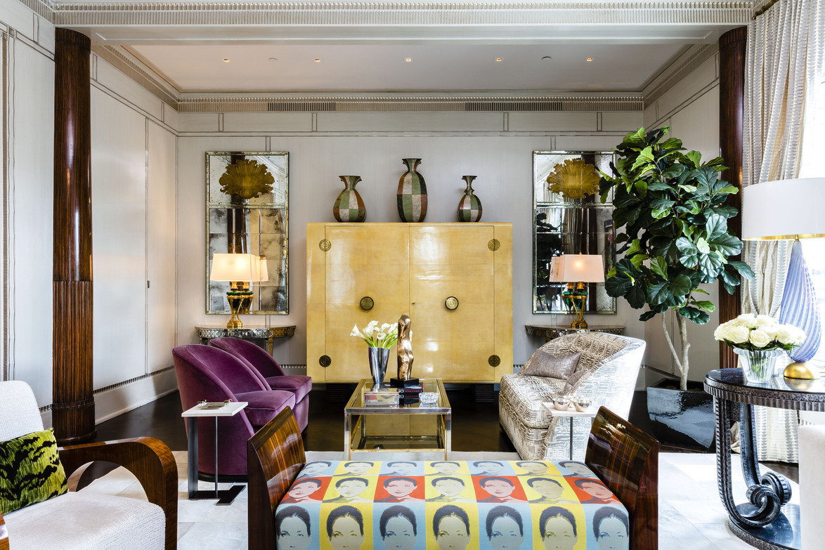 Elegant living room with eclectic decor, featuring velvet chairs, colorful pop art, decorative vases, and lush green plants.