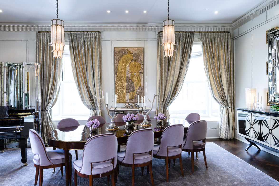 Elegant dining room with a large table, purple chairs, decorative curtains, and hanging chandeliers.