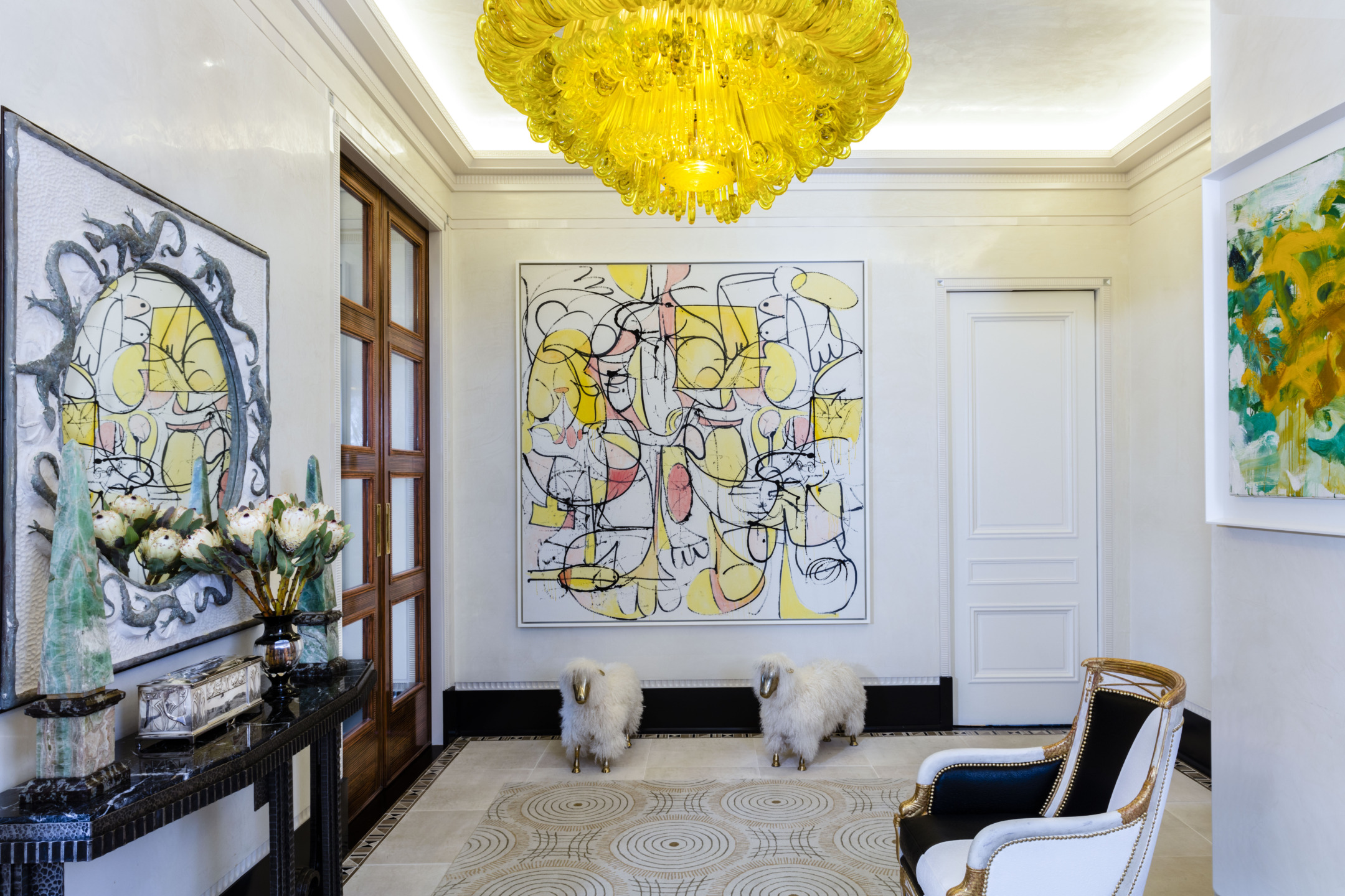 Elegant hallway with abstract art, yellow chandelier, ornate chair, decorative console table, and two white sheep sculptures.
