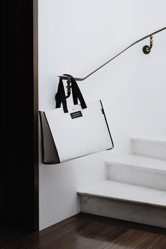 White and black tote bag with handles hanging on a railing beside a staircase.