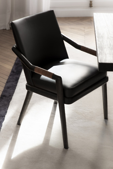 Black leather chair next to a wooden table in a sunlit room, featuring parquet flooring and a cozy rug.