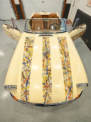 Classic convertible car with abstract paint design on hood and doors, viewed from above in a garage setting.