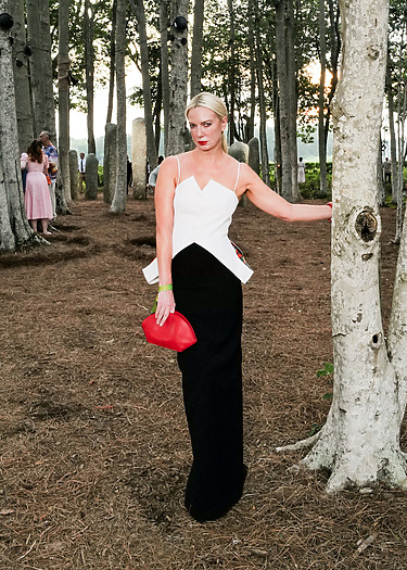 Person in a stylish dress posing in a wooded area with sunlight filtering through the trees.