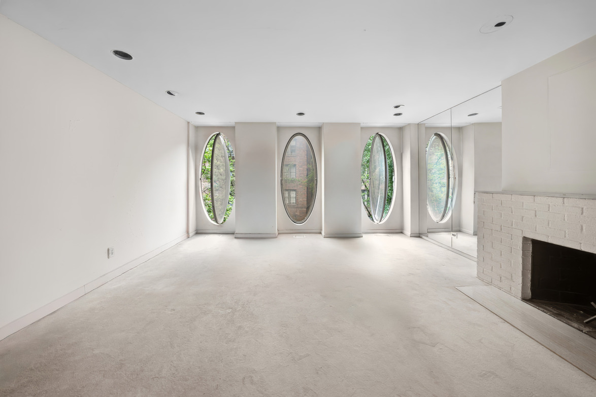 Spacious empty room with unique oval windows and a white brick fireplace, offering a modern and airy atmosphere.