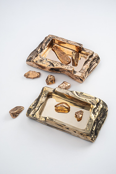 Two textured metallic trays with scattered bronze-colored stones on a white background.