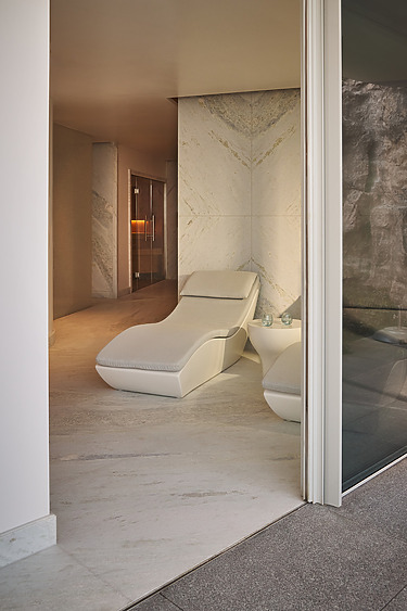 Minimalist spa room with a plush, modern lounge chair, soft lighting, and textured walls for a serene relaxation ambiance.