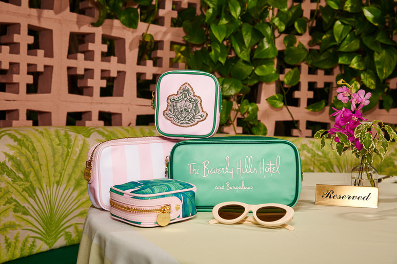 Assorted branded cosmetic bags on a table with sunglasses and flowers, set against a leafy backdrop.