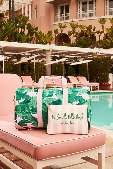 Tropical print luggage set on a pink lounge chair by a pool at a luxury hotel surrounded by palm trees.