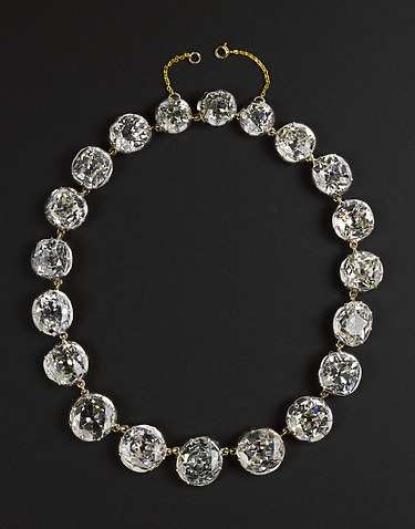 Gold necklace with large round diamond ornaments against a black background.