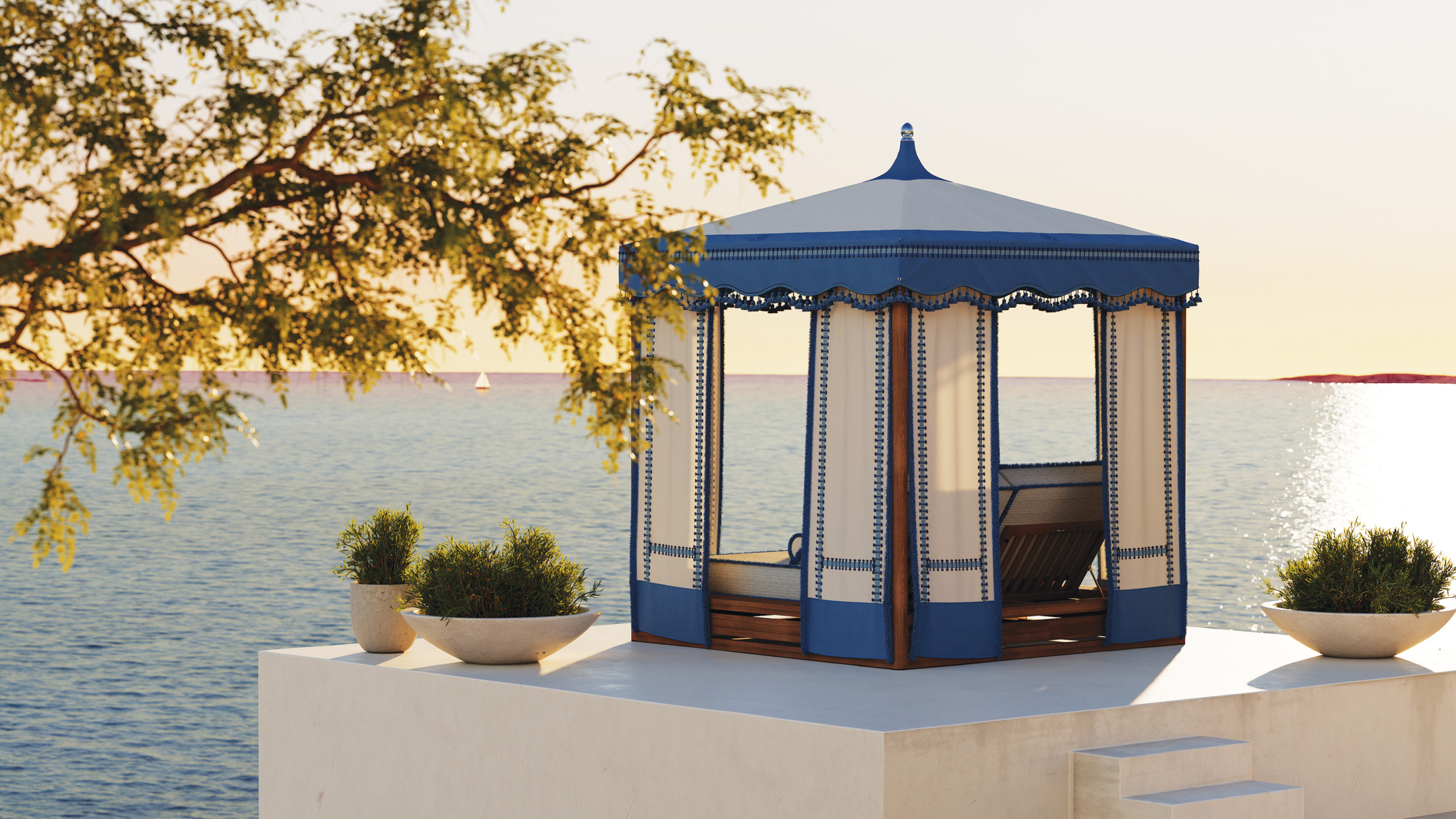 Blue gazebo on a white platform by the sea with potted plants and a tree, sunset in the background.
