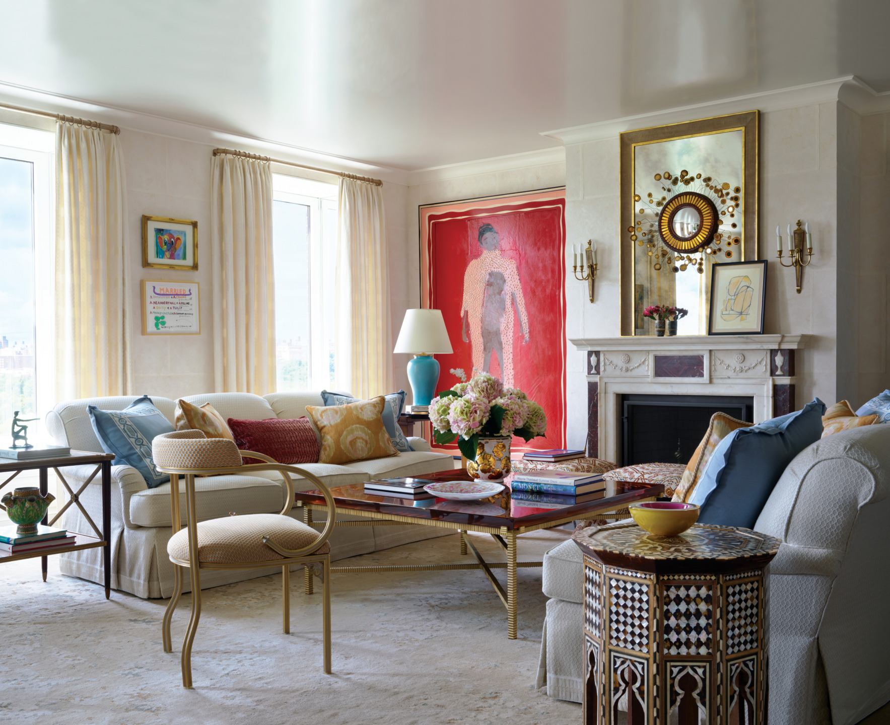 Elegant living room with sofas, colorful cushions, a coffee table, large framed artwork, and a fireplace with mirrored decor.