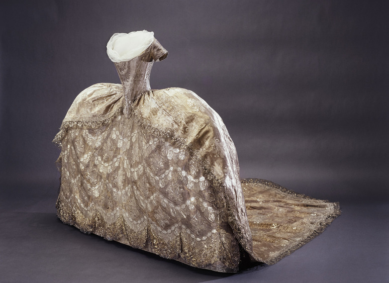 Intricately designed 18th-century gown with elaborate embroidery and voluminous skirt displayed against a dark background.