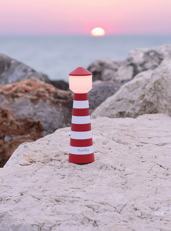 Red and white striped lighthouse-shaped lamp on rocks by the sea at sunset.