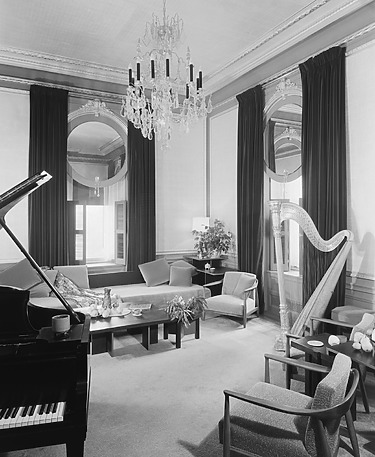 Elegant vintage living room with a grand piano, harp, chandelier, large windows with curtains, and comfortable seating.