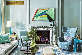 Modern living room with blue accents, abstract art above fireplace, stylish chandelier, and cozy seating area.
