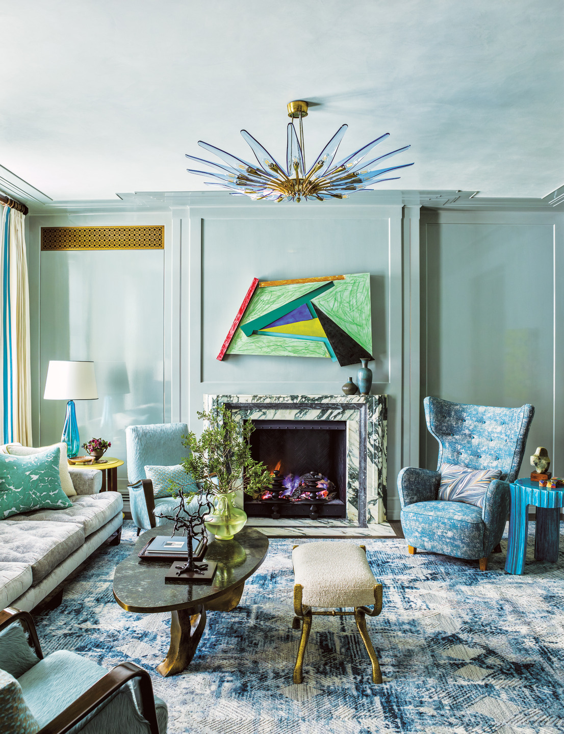 Modern living room with blue accents, abstract art above fireplace, stylish chandelier, and cozy seating area.
