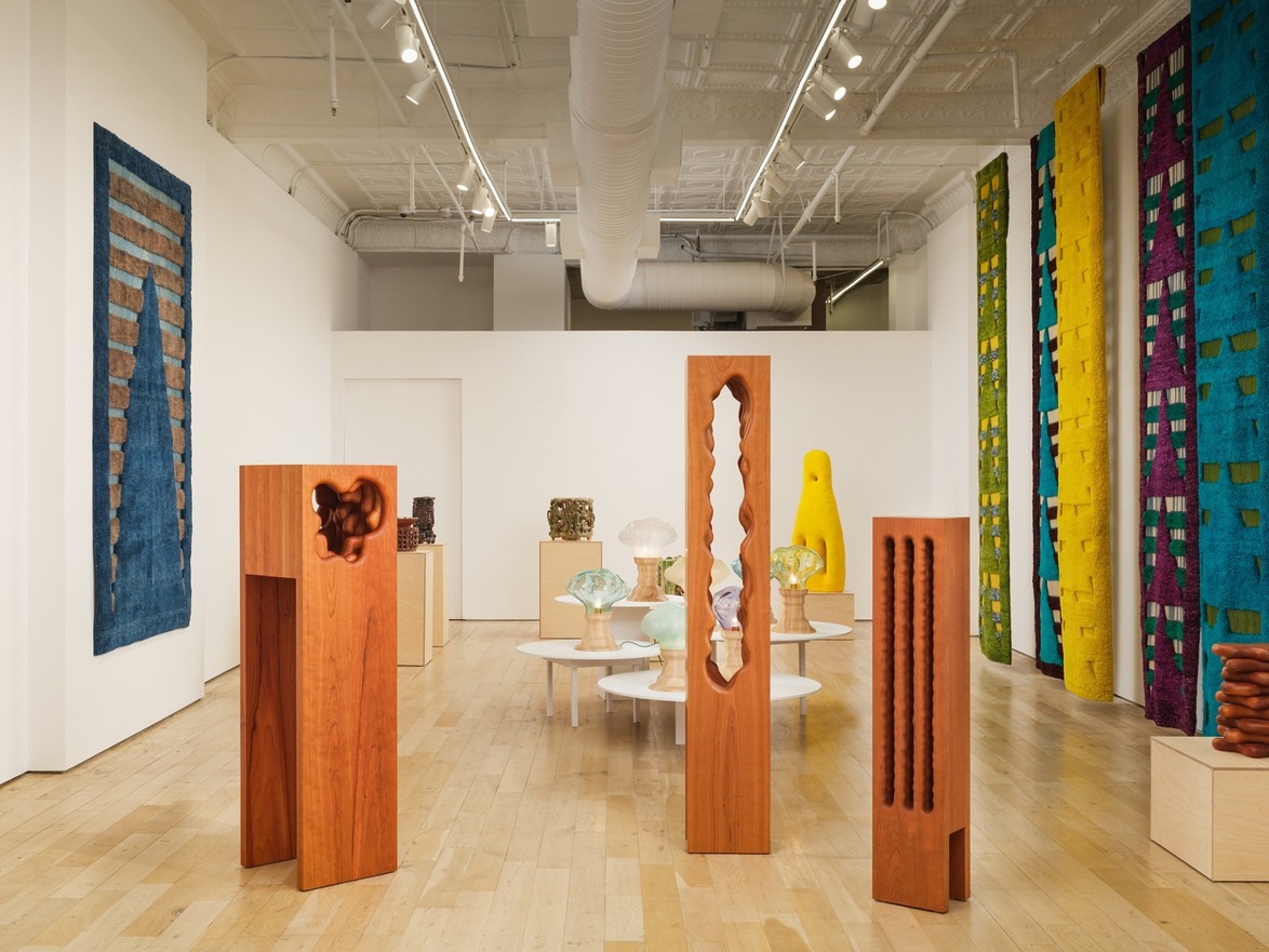 Gallery interior with wooden sculptures, colorful woven wall hangings, and various artistic glass pieces on display.