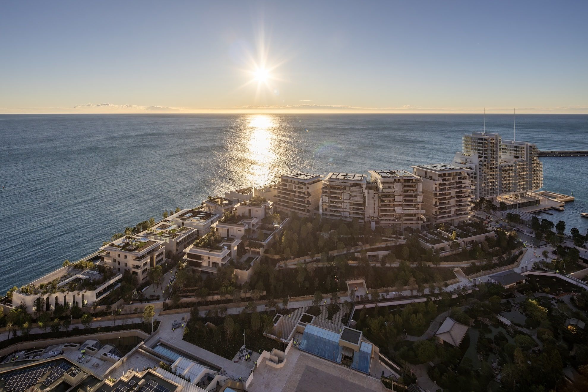 Aerial view of seaside cityscape with modern buildings and the sun setting over the ocean.