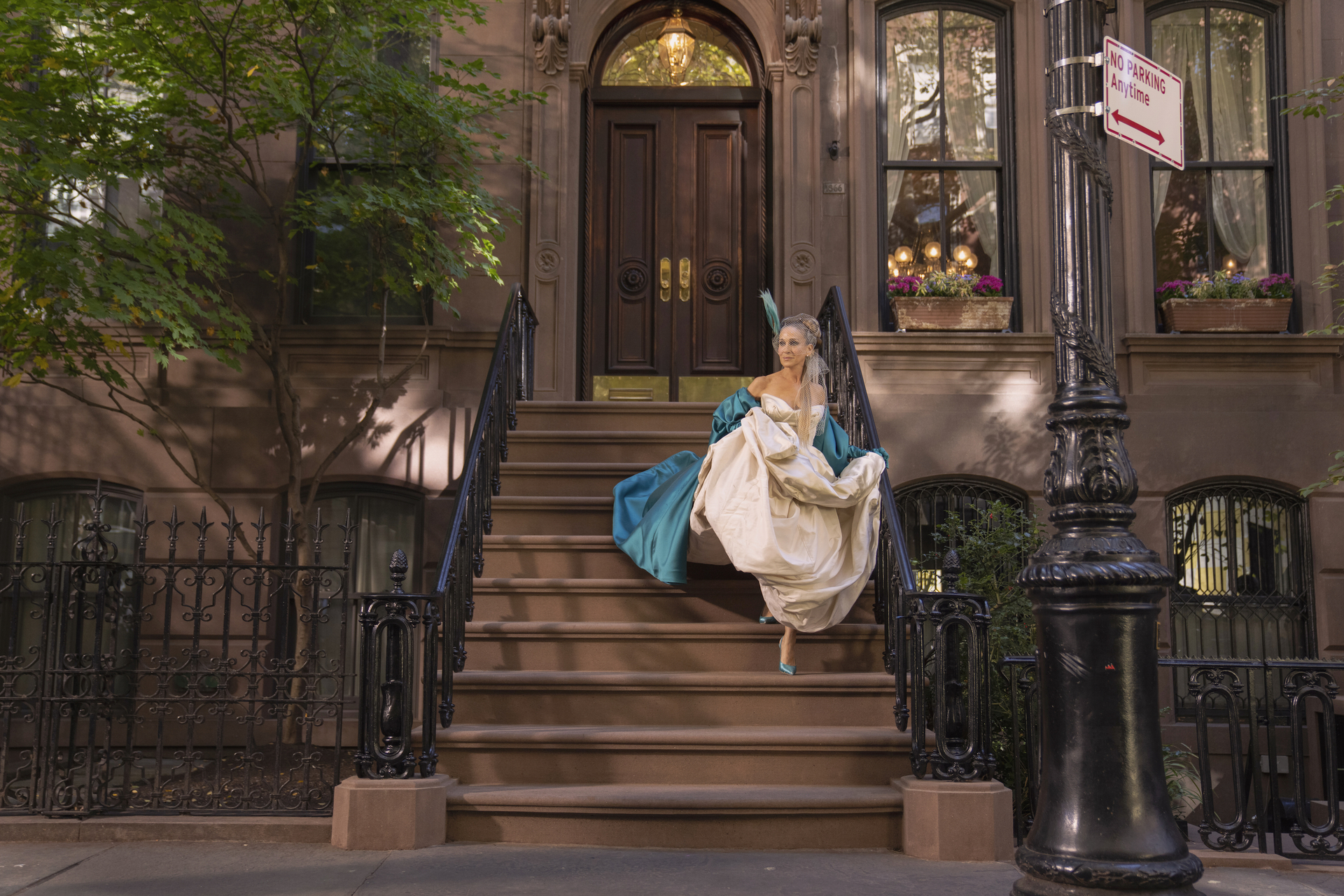 Woman in vintage dress descending brownstone stairs, vibrant teal and cream attire, urban setting with streetlight and trees.